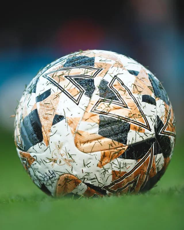 A match ball resting on grass, with grass clippings on its surface.
